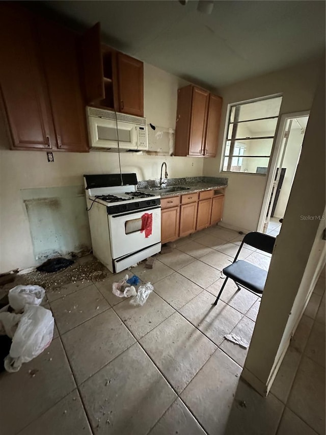 kitchen with brown cabinetry, white appliances, a sink, and light tile patterned floors