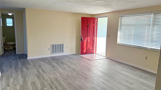 empty room with a textured ceiling, wood finished floors, visible vents, and baseboards