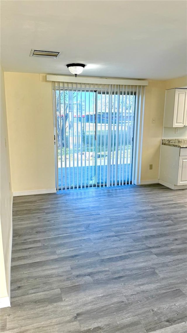 unfurnished living room with a healthy amount of sunlight, visible vents, baseboards, and wood finished floors