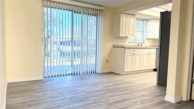 kitchen featuring baseboards, a sink, light wood-style flooring, and white cabinets