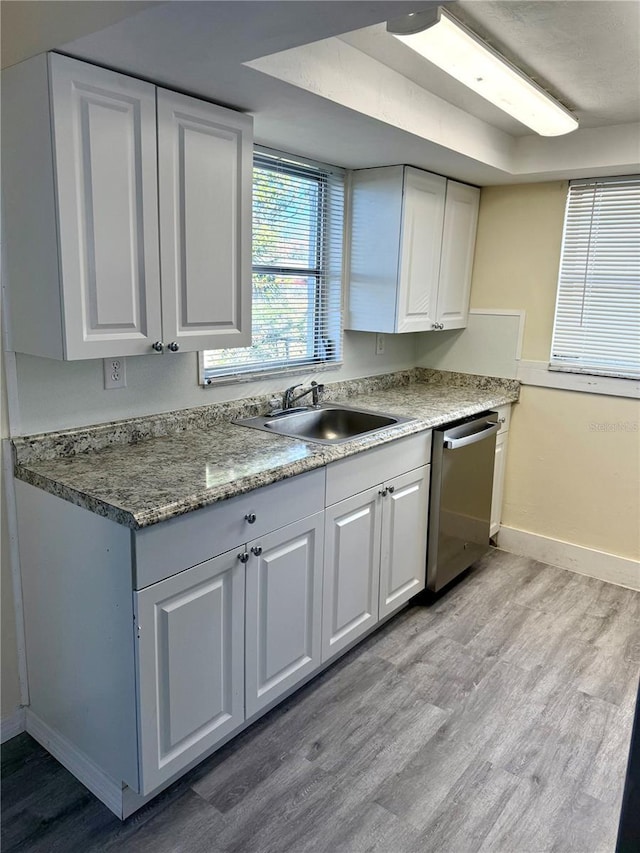 kitchen with light wood finished floors, stainless steel dishwasher, white cabinetry, a sink, and baseboards