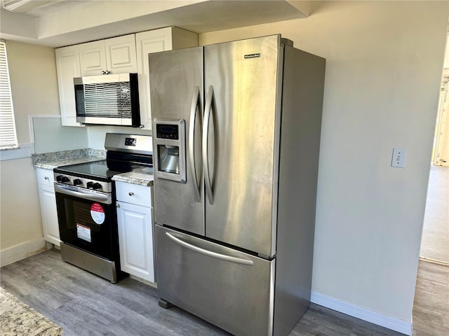 kitchen featuring stainless steel appliances, white cabinets, light wood-style flooring, and baseboards