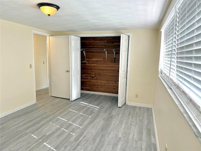 unfurnished bedroom featuring a closet, wooden walls, baseboards, and wood finished floors