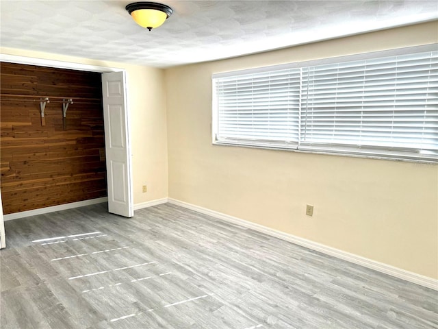 unfurnished bedroom with wood walls, wood finished floors, and baseboards