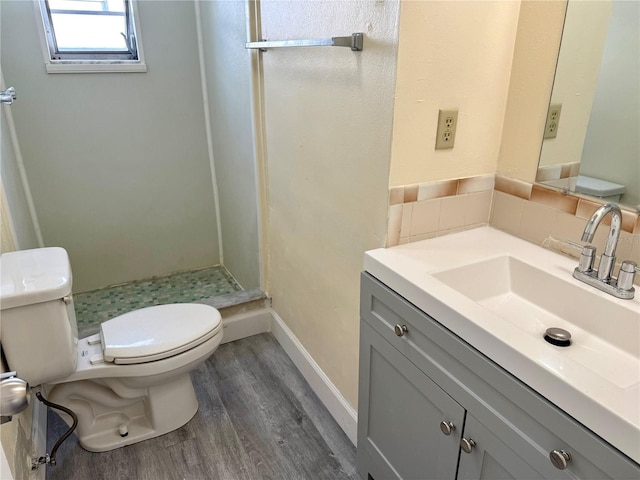 bathroom with toilet, wood finished floors, vanity, baseboards, and a stall shower