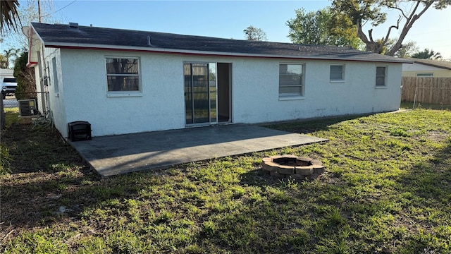 rear view of property featuring an outdoor fire pit, fence, a lawn, stucco siding, and a patio area