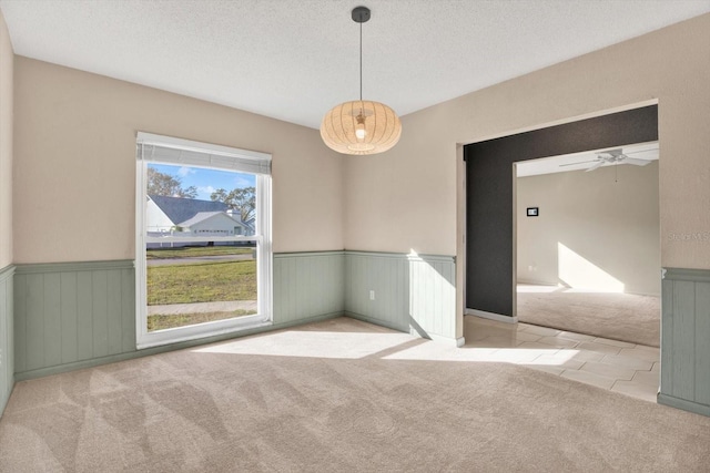 unfurnished room featuring a textured ceiling, carpet flooring, and wainscoting