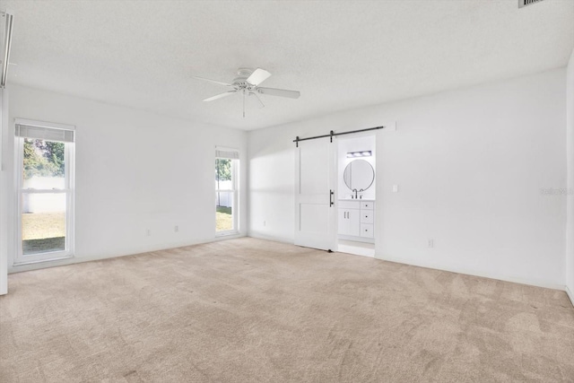 unfurnished room with a textured ceiling, carpet floors, a barn door, and a ceiling fan