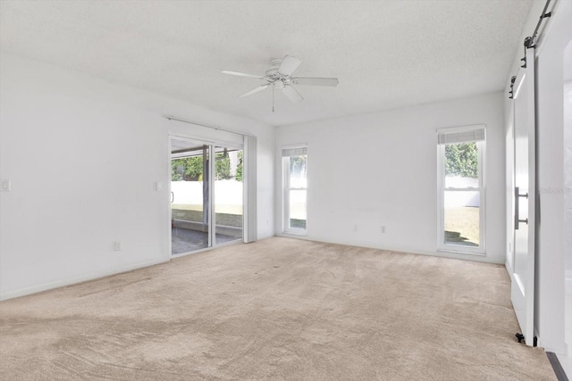 unfurnished room with a barn door, a ceiling fan, a wealth of natural light, and light colored carpet