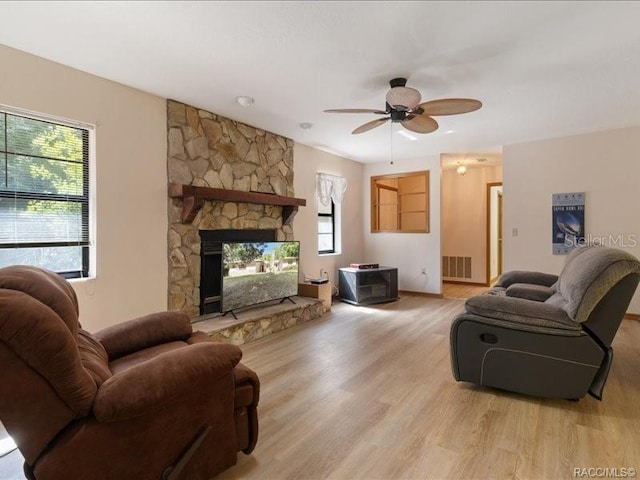 living area with ceiling fan, a stone fireplace, light wood-style flooring, and visible vents