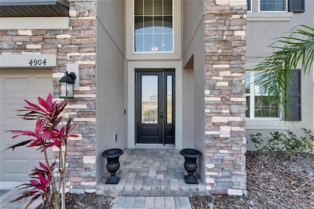 view of exterior entry with a garage, stone siding, and brick siding