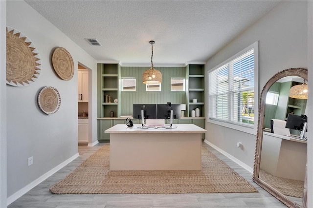 office with built in shelves, baseboards, visible vents, light wood finished floors, and a textured ceiling