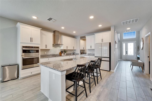 kitchen with visible vents, double oven, freestanding refrigerator, wall chimney exhaust hood, and a sink