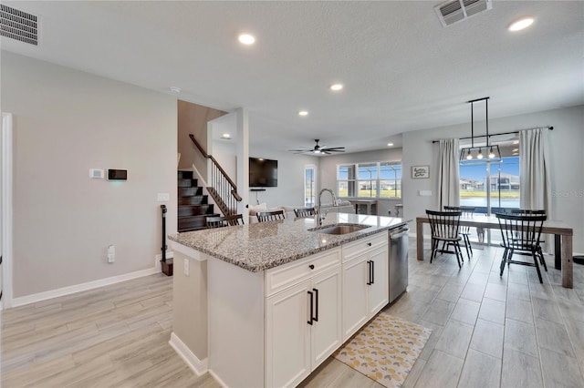 kitchen featuring a sink, visible vents, light stone countertops, and a kitchen island with sink