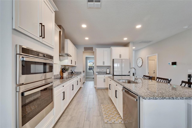 kitchen featuring a sink, wall chimney range hood, visible vents, and stainless steel appliances