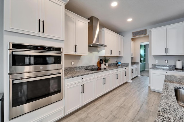 kitchen with white cabinetry, light wood-style floors, double oven, wall chimney exhaust hood, and black electric stovetop