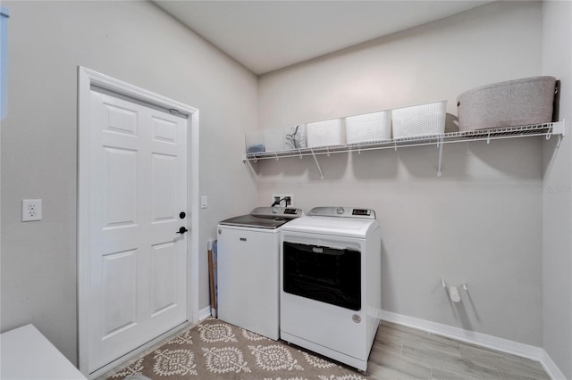 clothes washing area with washer and dryer, laundry area, light wood-style floors, and baseboards