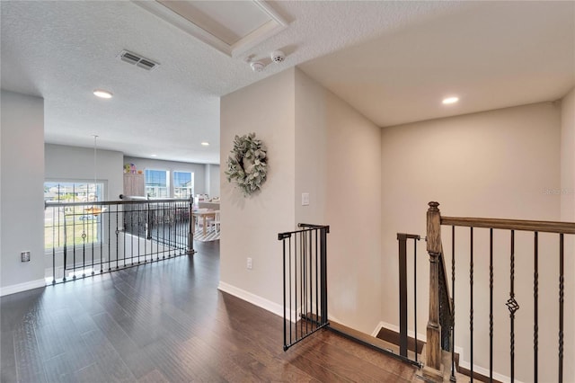 corridor featuring an upstairs landing, a textured ceiling, baseboards, and wood finished floors