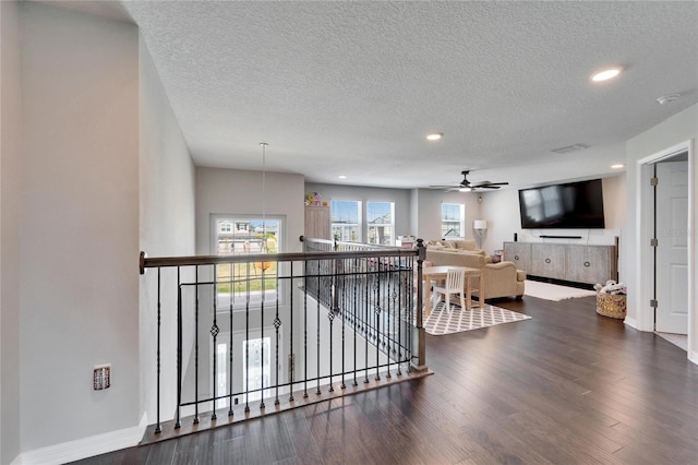 hall with an upstairs landing, a textured ceiling, wood finished floors, recessed lighting, and baseboards