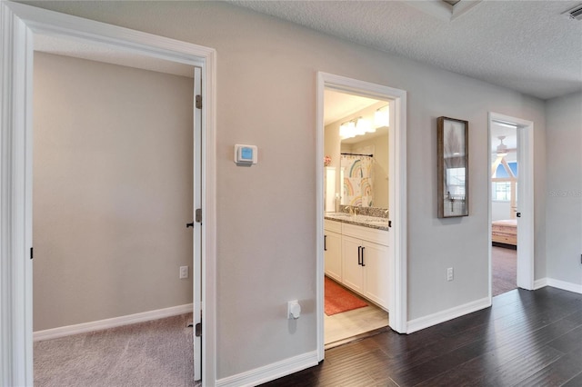 hallway featuring baseboards, visible vents, dark wood-style flooring, a sink, and a textured ceiling