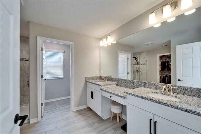 bathroom featuring a walk in closet, visible vents, a stall shower, a textured ceiling, and baseboards