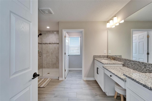 bathroom with visible vents, baseboards, vanity, a stall shower, and a textured ceiling