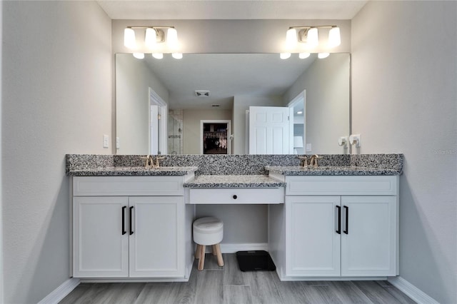 bathroom featuring baseboards, two vanities, wood finished floors, and a shower stall