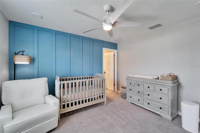 bedroom with visible vents, a crib, a textured ceiling, carpet flooring, and a decorative wall