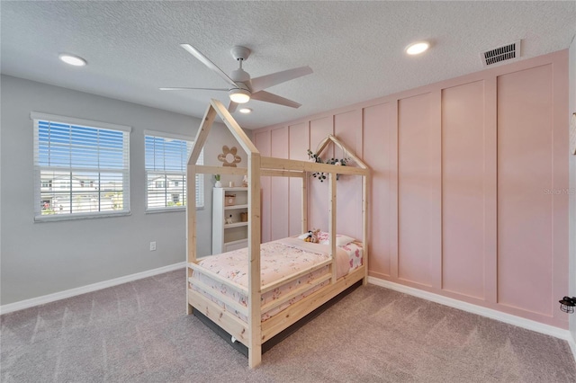 bedroom featuring a decorative wall, light colored carpet, visible vents, and a textured ceiling