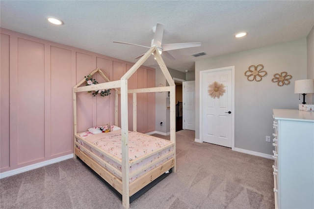 bedroom with visible vents, light carpet, a textured ceiling, recessed lighting, and a decorative wall