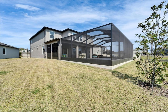 rear view of house featuring a lawn, glass enclosure, and stucco siding