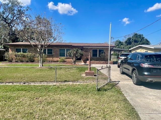 ranch-style home featuring a fenced front yard, an attached carport, concrete driveway, and a front yard