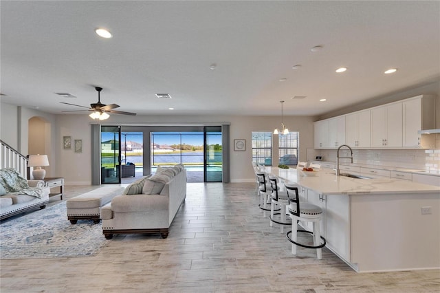 kitchen with arched walkways, a sink, white cabinetry, open floor plan, and decorative backsplash