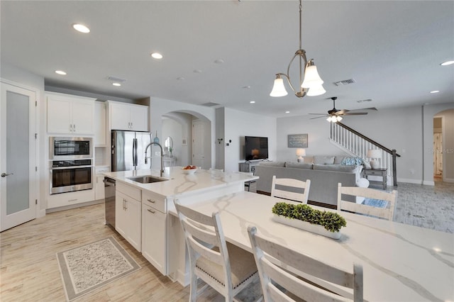 kitchen featuring arched walkways, stainless steel appliances, visible vents, open floor plan, and a sink