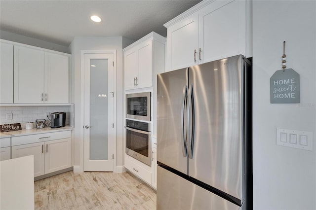 kitchen featuring light wood finished floors, decorative backsplash, appliances with stainless steel finishes, light countertops, and white cabinetry