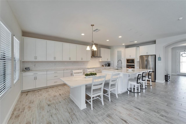 kitchen featuring visible vents, a large island, stainless steel appliances, wall chimney range hood, and a sink