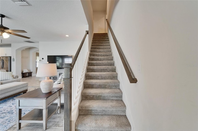 stairway featuring arched walkways, ceiling fan, a textured ceiling, visible vents, and baseboards