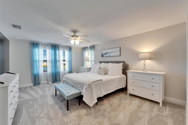 bedroom with baseboards, light carpet, visible vents, and a textured ceiling