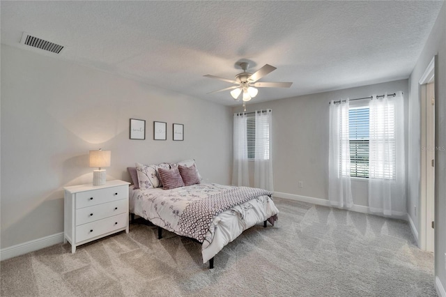 bedroom featuring baseboards, visible vents, a ceiling fan, light colored carpet, and a textured ceiling