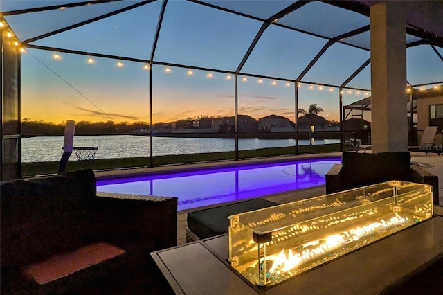 pool at dusk with a patio, a water view, and a lanai