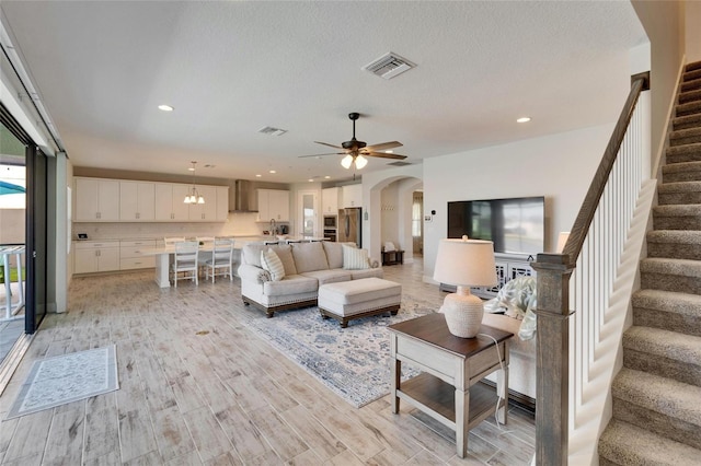 living area featuring light wood-style floors, arched walkways, visible vents, and stairs