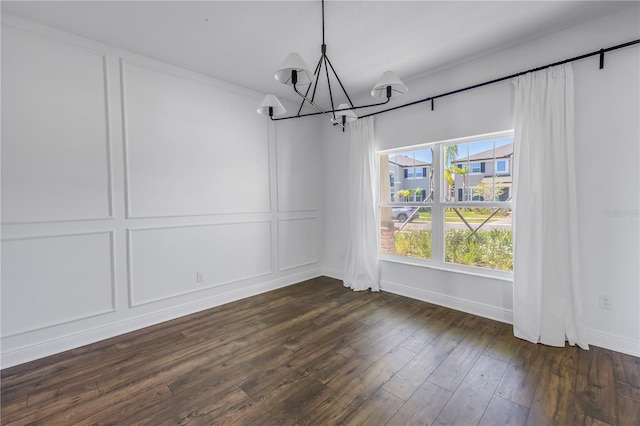 unfurnished dining area with an inviting chandelier, baseboards, a decorative wall, and dark wood finished floors