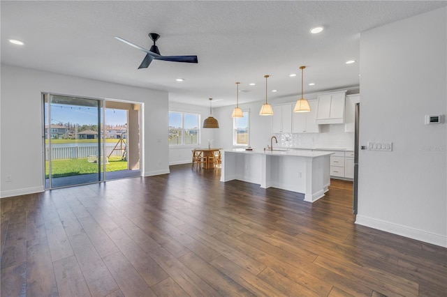 unfurnished living room with dark wood-style flooring, a sink, baseboards, and ceiling fan