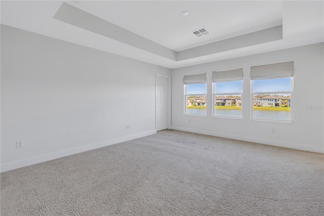 unfurnished room featuring a tray ceiling, light colored carpet, visible vents, and baseboards