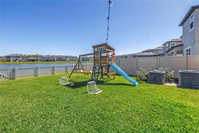 view of jungle gym featuring a yard, central AC unit, a water view, and a fenced backyard