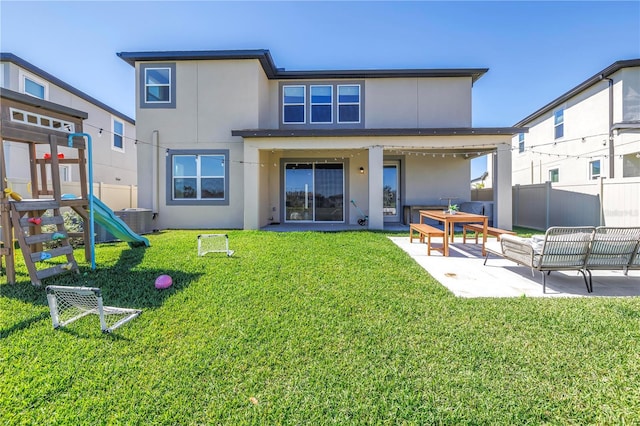 back of property with a playground, fence, a lawn, and stucco siding