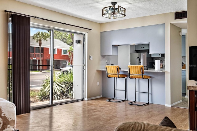 kitchen with a textured ceiling, a breakfast bar area, visible vents, gray cabinets, and freestanding refrigerator