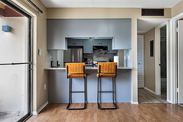 kitchen with light wood-type flooring, freestanding refrigerator, visible vents, and gray cabinetry