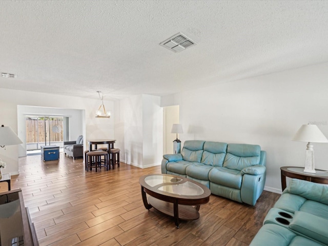 living room with visible vents, a textured ceiling, an inviting chandelier, and wood finished floors