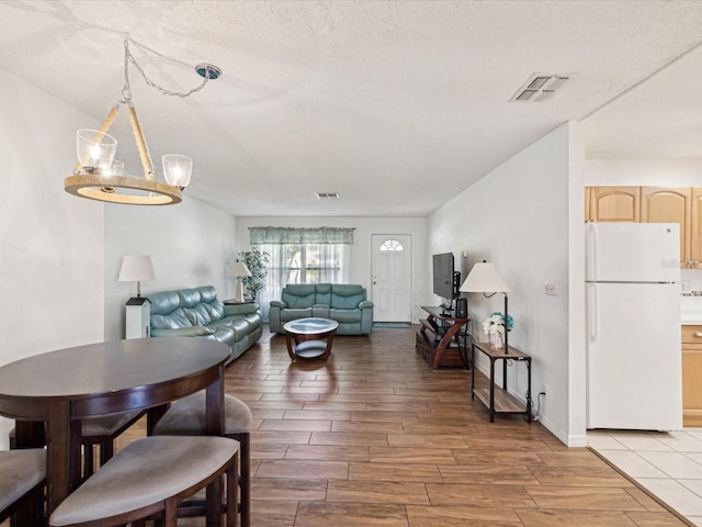 living area featuring wood finish floors, visible vents, a textured ceiling, and an inviting chandelier